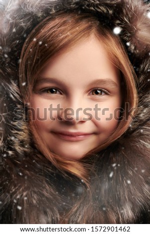Christmas winter kids fashion. Close up portrait of smiling little girl in fur hood. Winter fur fashion for kids.