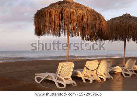 Sea morning landscape. To the right of sun umbrellas and deck chairs on the sandy beach in the early morning. Without people, horizontal, cropped shot. Concept of tourism and the beauty of nature.