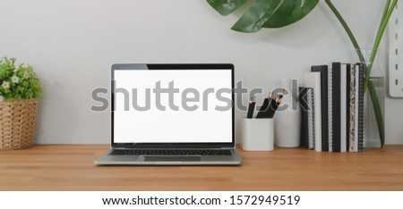 Cropped shot of comfortable workplace with laptop computer and office supplies on wooden table background and white wall background