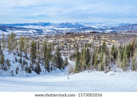 View of Colorado, USA, ski slope descending to resort town in winter; distant mountains and blue sky in background; view from the top of the slope Royalty-Free Stock Photo #1573001056