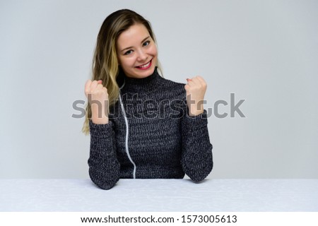 Concept of a talking woman sitting at a table in front of the camera. Photo of a pretty smiling girl with curly hair with emotions in a gray dress on a white background.