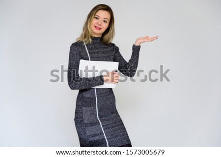 Concept of a talking business woman facing the camera. Photo of a pretty smiling girl with curly hair with emotions in a gray dress on a white background with a folder in her hands.