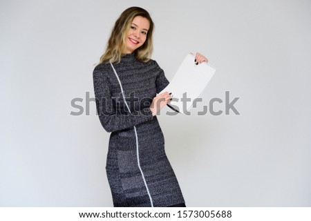 Concept of a talking business woman facing the camera. Photo of a pretty smiling girl with curly hair with emotions in a gray dress on a white background with a folder in her hands.