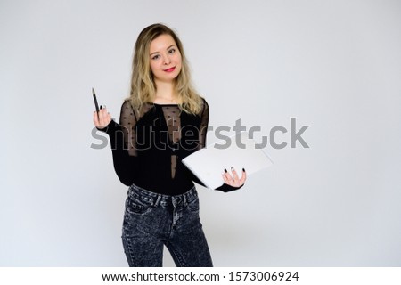 Concept of a woman talking to the camera. A photo of a pretty smiling girl with curly hair in a black T-shirt on a white background is standing right in front of the camera with a folder in her hands.