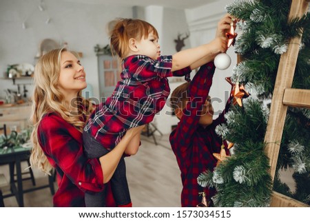 Beautiful mother in a red shirt. Family standing in a room. Little girl and boy near christmas tree