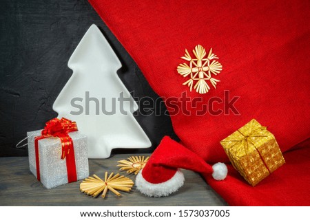 Festive red Christmas still life with gifts, handmade straw snow flakes, white Xmas tree and a Santa hat over colorful bright red fabric to celebrate the holiday season, free copy space