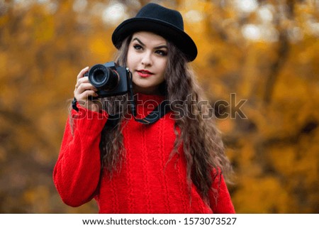 Beautiful young woman with modern photo camera in autumn park