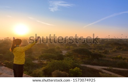 Woman watching sunrise with many hot air balloons above Bagan in Myanmar. Bagan is an ancient city with thousands of historic buddhist temples and stupas.