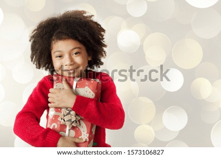 Festive Christmas concept. Happy adorable african american child girl with christmas gift in hands on light background.