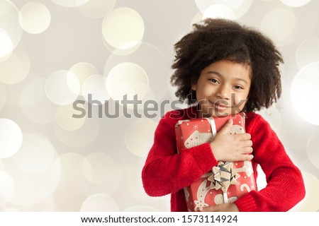 Christmas concept. Happy adorable african american child girl with christmas gift in hands on light background.