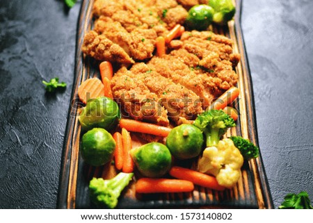Chicken breast on a dark background. Roasted chicken fillet with vegetables on a wooden board. Brussels sprouts, carrots, baked meat. Top view 