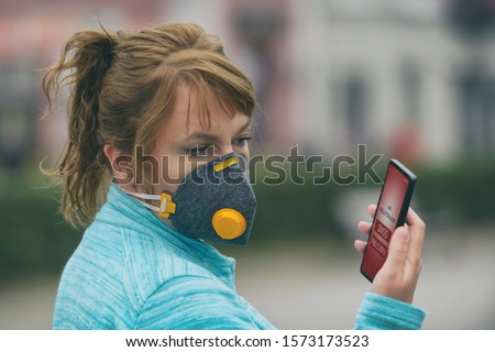 Woman wearing a real anti-pollution, anti-smog and viruses face mask and checking current air pollution with smart phone app Royalty-Free Stock Photo #1573173523
