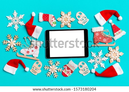 Top view of digital tablet with Christmas decorations and Santa hats on blue background. Happy holiday concept.