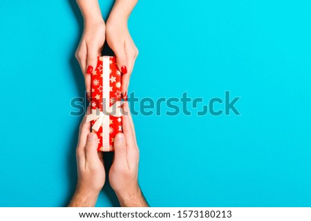 Top view of male and female hands holding present box on colorful background. Sharing a gift concept. Close up.