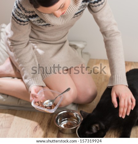 Beautiful young woman feeding her cat at home