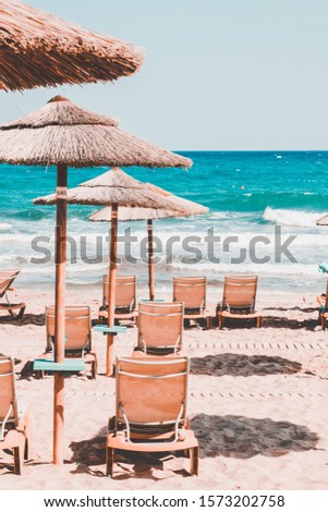 Empty sunbeds and straw umbrellas on the beach. Holidays at Aegean Sea of Crete, Greece. Popular tourist destination
