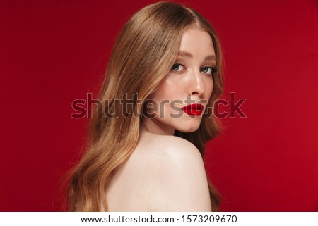 Image of a serious young pretty caucasian woman posing isolated over red wall background with bright red lipstick.