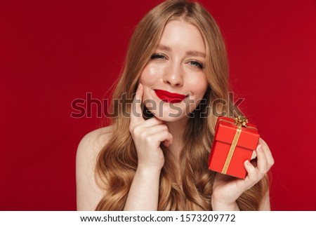 Image of young positive happy cheery woman posing isolated over red wall background with bright red lipstick holding christmas present gift.