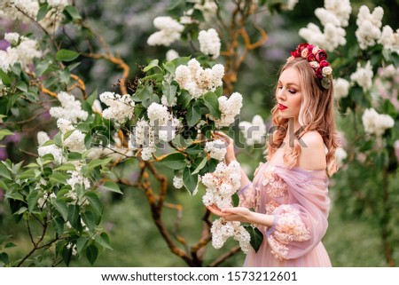 Beautiful romantic fairy girl in long dress in blooming spring garden. Gorgeous young model with perfect hairstyle in fairy forest. Fantasy art