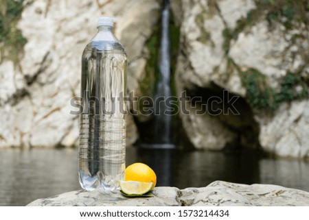 Bottle of drinking water with lemon on the background of a mountain stream
