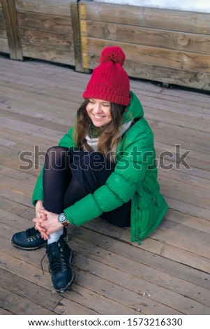Woman hipster in bright clothes laughing and smiling. Young happy girl in a red knit hat, green jacket, grey scarf, yellow small bag. Women's fashion.