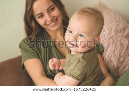 Home portrait of a baby boy with mother on the bed. Mom holding and kissing her child. Mother day concept