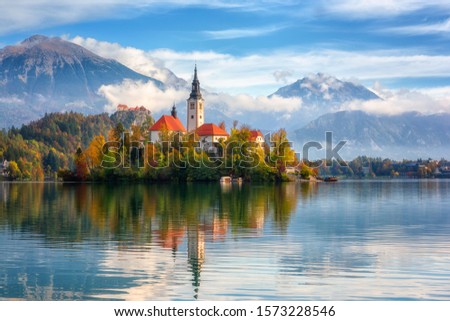 Famous alpine Bled lake (Blejsko jezero) in Slovenia, amazing autumn landscape. Scenic view of the lake, island with church, Bled castle, mountains and blue sky with clouds, outdoor travel background Royalty-Free Stock Photo #1573228546