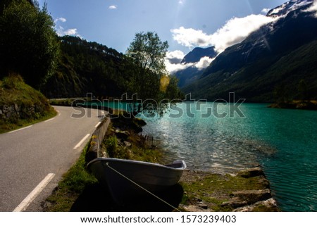 Small boat on beautiful Lovatnet Lake in Norway.  The water is turquoise because it is fed from a glacier.  There is a road along the lake. Beautiful nature background