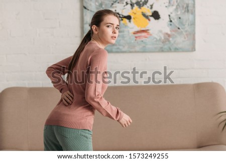 young woman looking at camera while suffering from back pain