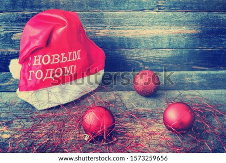 Father Christmas cap. Sparkling shiny Christmas red baubles and tinsel. On the cap is written in Russian - Happy New Year. Vintage wooden background