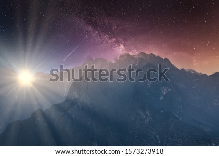 Night sky with milky way and bright sun with silhouettes of rocky mountains in the background. Abstract concept of day and night amalgamated into one picture.  No recognizable buildings or people. 