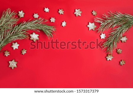 A Christmas homemade gingerbread cookies in the form of a snowflake sprinkled with icing sugar hanging around a pine branch with hoarfrost. Flat lay on red background with copy space.