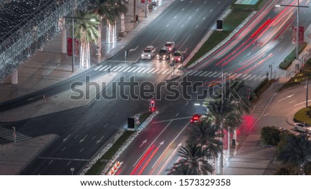 Aerial view of intersection with many transports in traffic and modern walking alley with palms night timelapse in Dubai Downtown, Dubai, United Arab Emirates