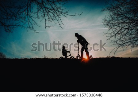 silhouette of father and little daughter riding bike and scooter at sunset