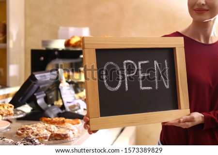 Female business owner holding OPEN sign in bakery, closeup