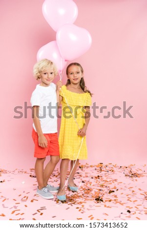 smiling and cute kids holding balloons on pink background 