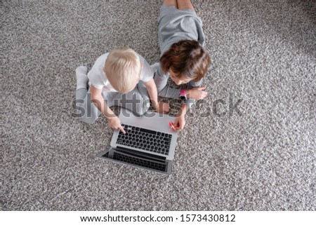 Top view brother and sister are watching cartoon on laptop while lying on floor in children's room. Concept of friendly enthusiastic smart little children. Children and social addiction. Copyspace