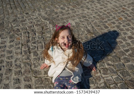 The girl put a piece of jewelry on the head of a cat's ears. Hoop cat ears. Girl with blond long hair. A series of photos with a girl of 9 years. Child on a walk in the park. schoolgirl on a walk