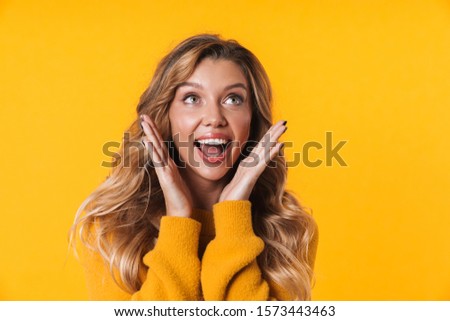 Image of delighted blonde woman with long hair wearing warm sweater smiling and looking upward isolated over yellow background