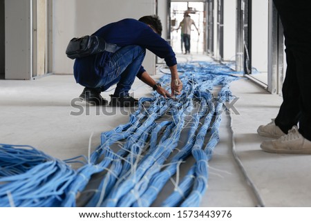Worker wiring LAN cable at construction site. Unfinished Installation network system. Royalty-Free Stock Photo #1573443976