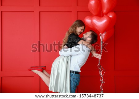 Happy young couple with heart-shaped balloons on color background. Valentine's Day celebration Royalty-Free Stock Photo #1573448737