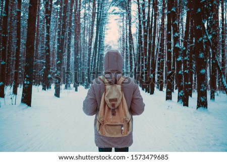 young man in a winter outfit standing in the middle of a winter snowy forest. Beautiful winter day, pine tree forest. The concept of winter travel and walks in the woods