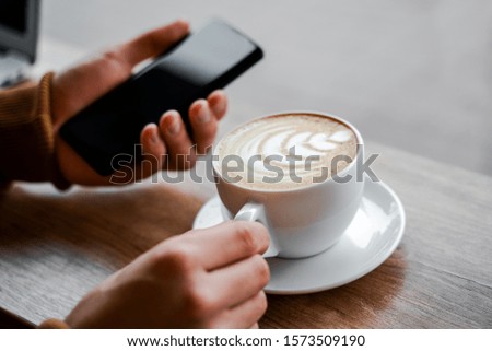 
Cropped image of male hands holding a black mobile phone with a blank screen on the hip and a white coffee cup in a cafe. Distance work, communication online, internet education, banking or booking