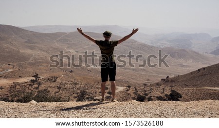 the man with arms spread looks at the endless desert from the viewpoint                  