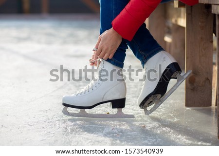 A girl is tying shoelaces on figured white skates on an ice rink