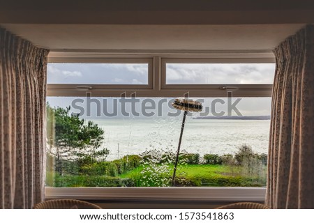 A double glazed picture window with small top light opening windows being cleaned with an extension brush and pure water. Some motion blur showing the movement of the brush. There is a sea view.