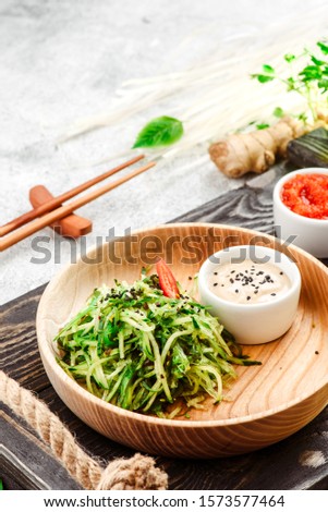 Pan-Asian food. Vegetable salad with chuka, cucumber and sesame seeds  in a beautiful wooden plate on a dark rustic tray on a light concrete background. Beautiful composition. Close-up. Space
