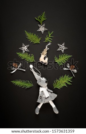 Christmas tree made from green natural branches with a mouse, New Year's toys, cones, bows and stars on a black background. Flat lay.