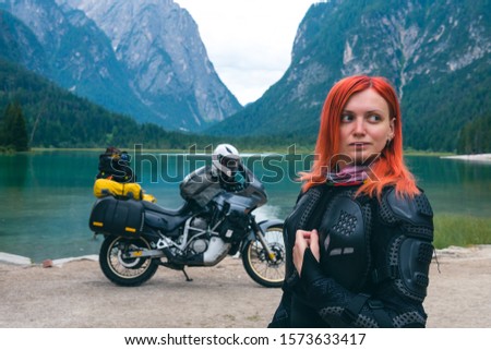 Close up portrait of female motobiker in protective turtle jacket. Touring motorcycle background. Extreme vacation, motorcyclist adventure lifestyle. Toblacher See, (Italian: Lago di Dobbiaco) Italy.