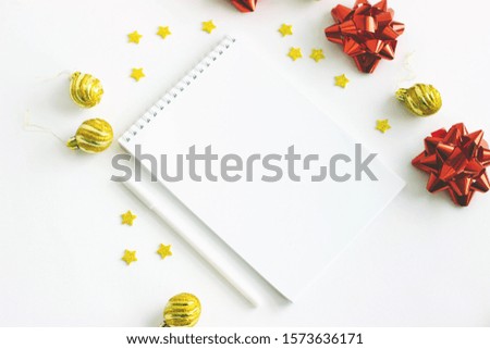 A notebook on an isolated white background. Golden Christmas balls, stars, three red shiny bows. Notepad with goals for 2020. Selective focus.
